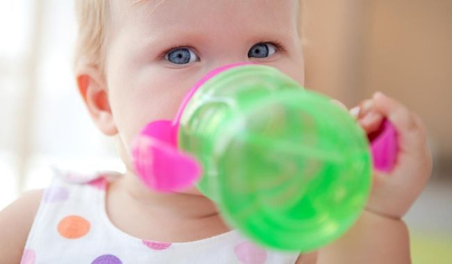 Bebe bebendo agua em um copo de transicao