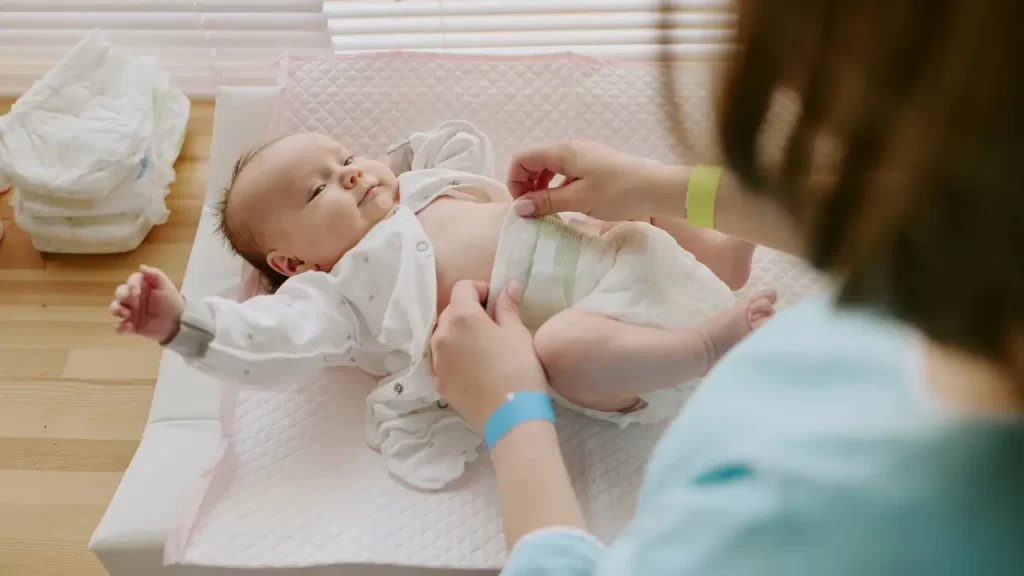 Quantas fraldas um bebê usa? Veja o consumo por idade Mulher colocando fralda em neném e representando quantas fraldas em bebe usa
