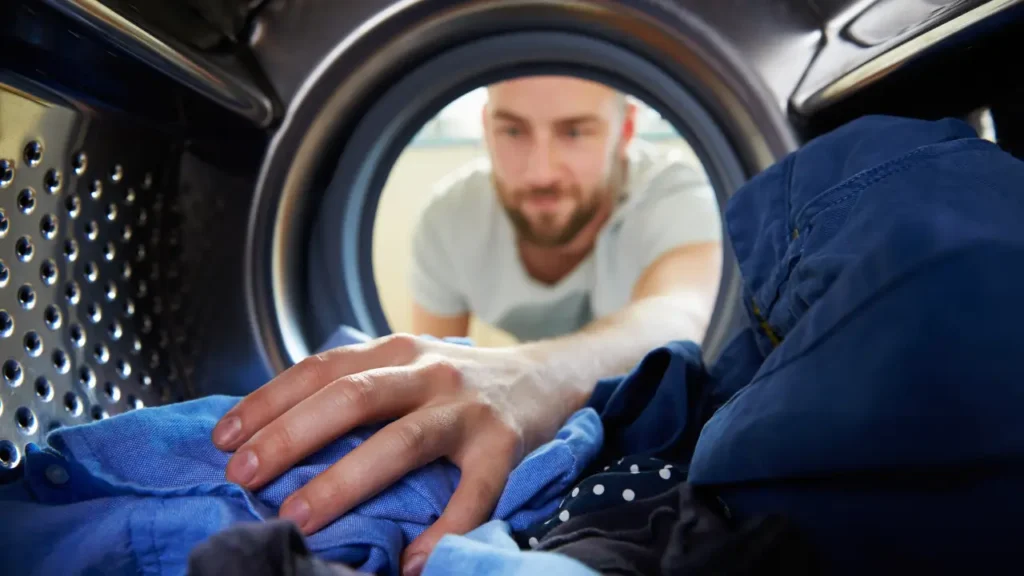Pessoas colocando roupas na máquina de lavar para tirar cheiro de suor da roupa.