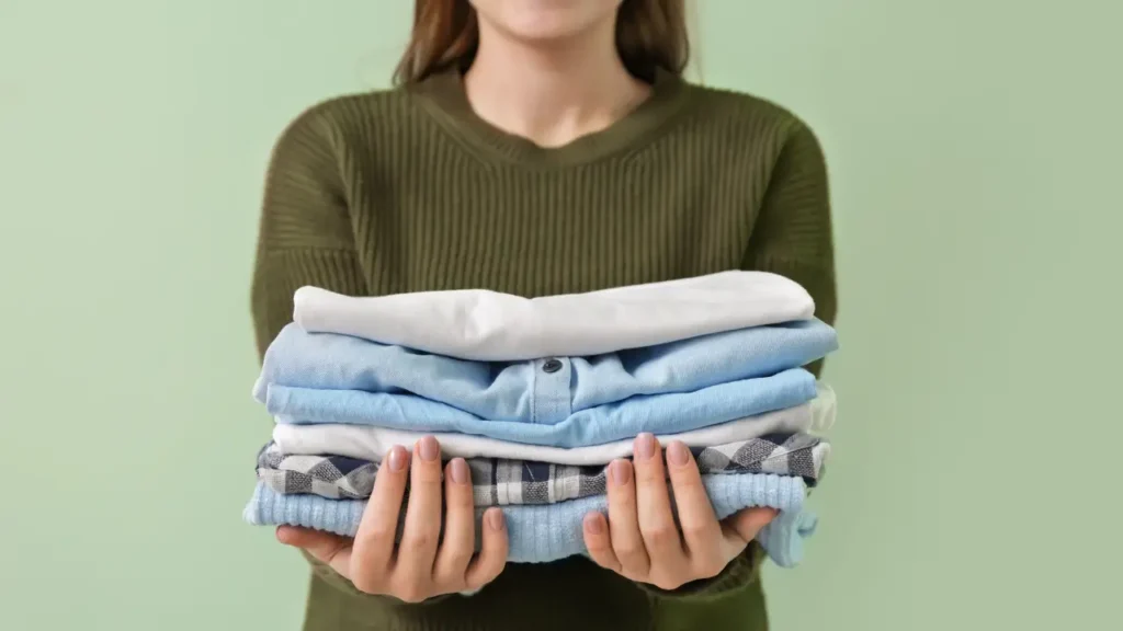 Mulher segurando pilha de roupas dobradas.