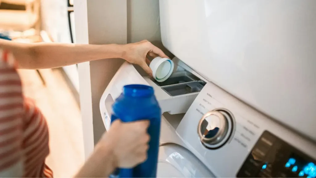 Pode lavar roupa com detergente neutro? Veja quando usar Uma pessoa colocando detergente neutro na maquina de lavar