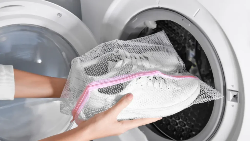 Uma pessoa colocando um par de tenis para lavar em maquina de lavar roupas